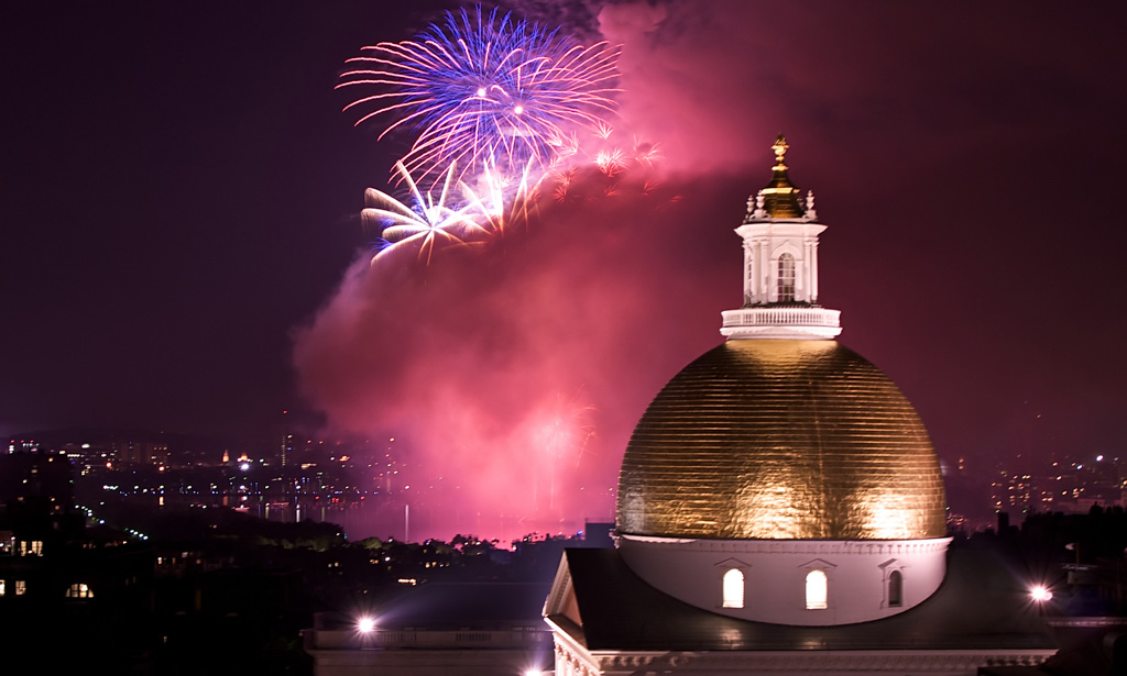 fourth of july fireworks explode in the sky over the charles river with the massachusetts state house in the foreground