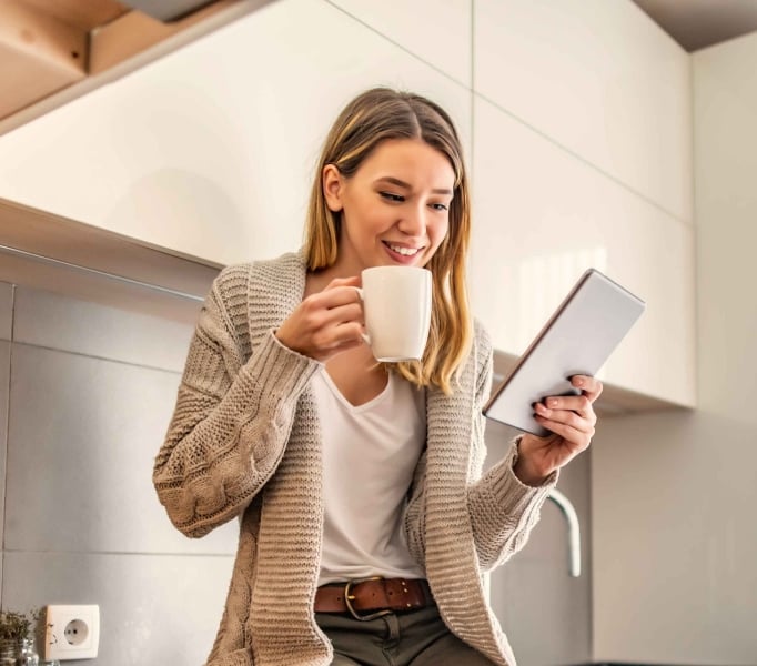 A mom stands drinking a cup of coffee and reading a daily planner