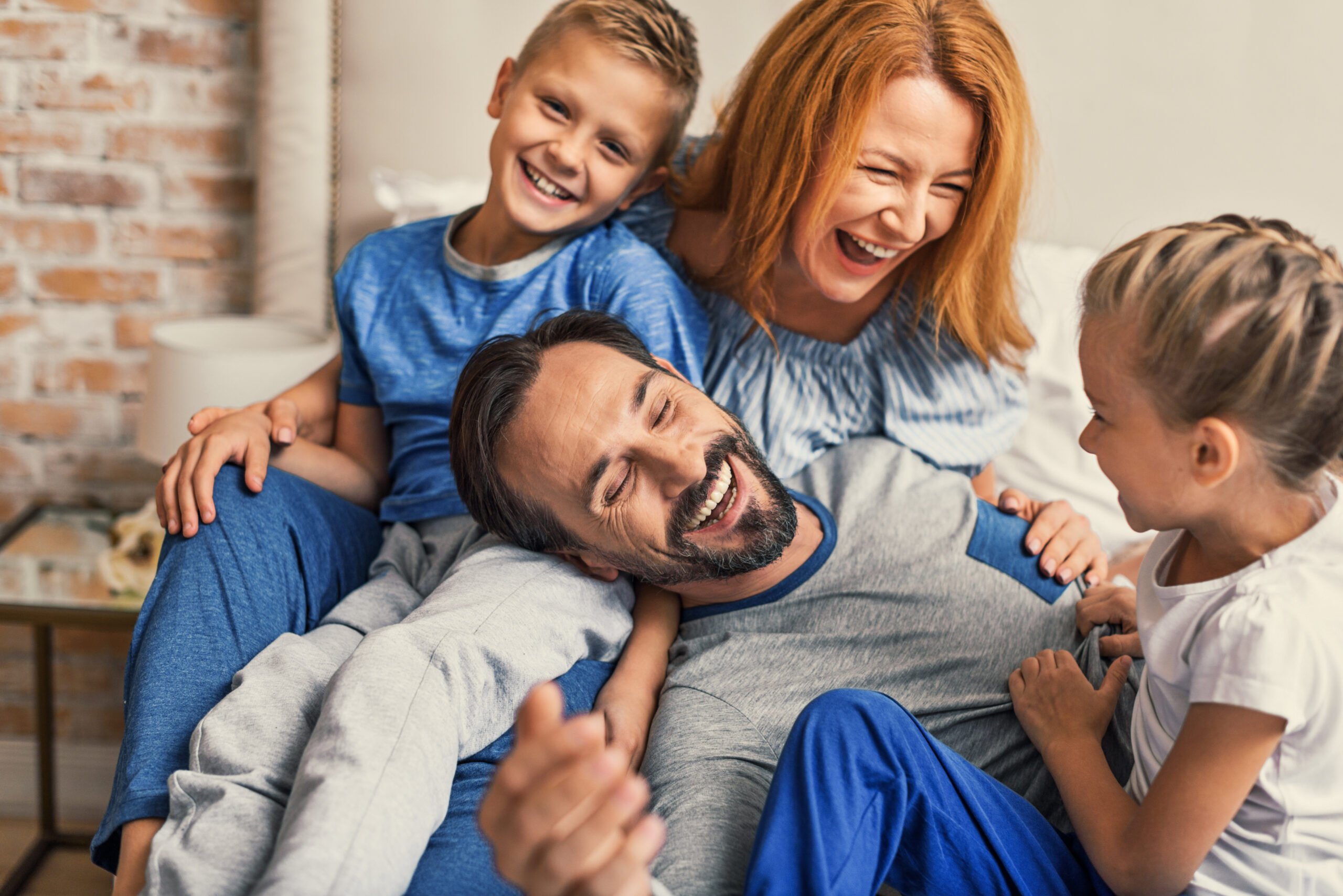 Family life is about fun. young smiling family of four having fun while lying on bed and hugging each other