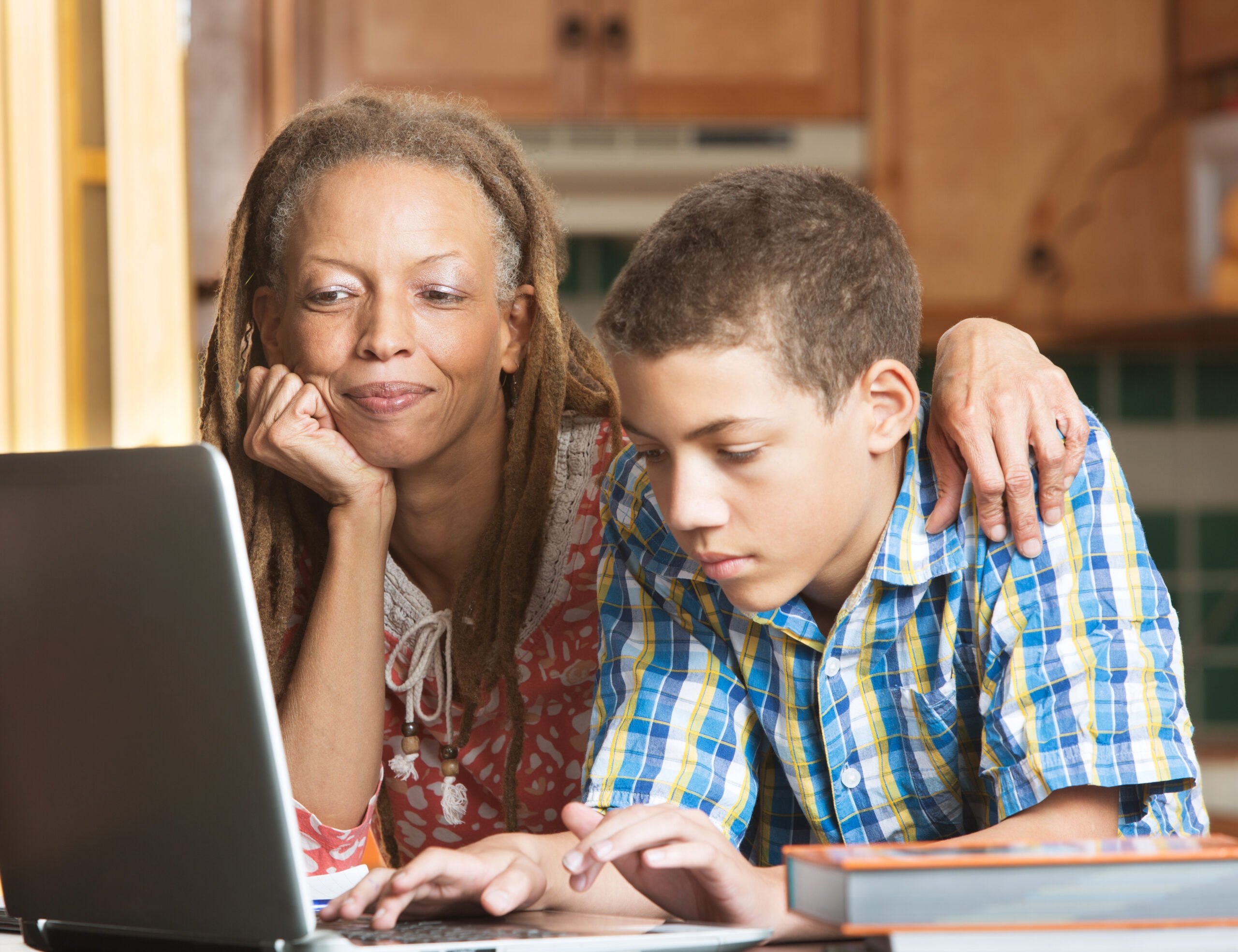 Mother overlooks as her teenaged son uses his laptop to study in their kitchen