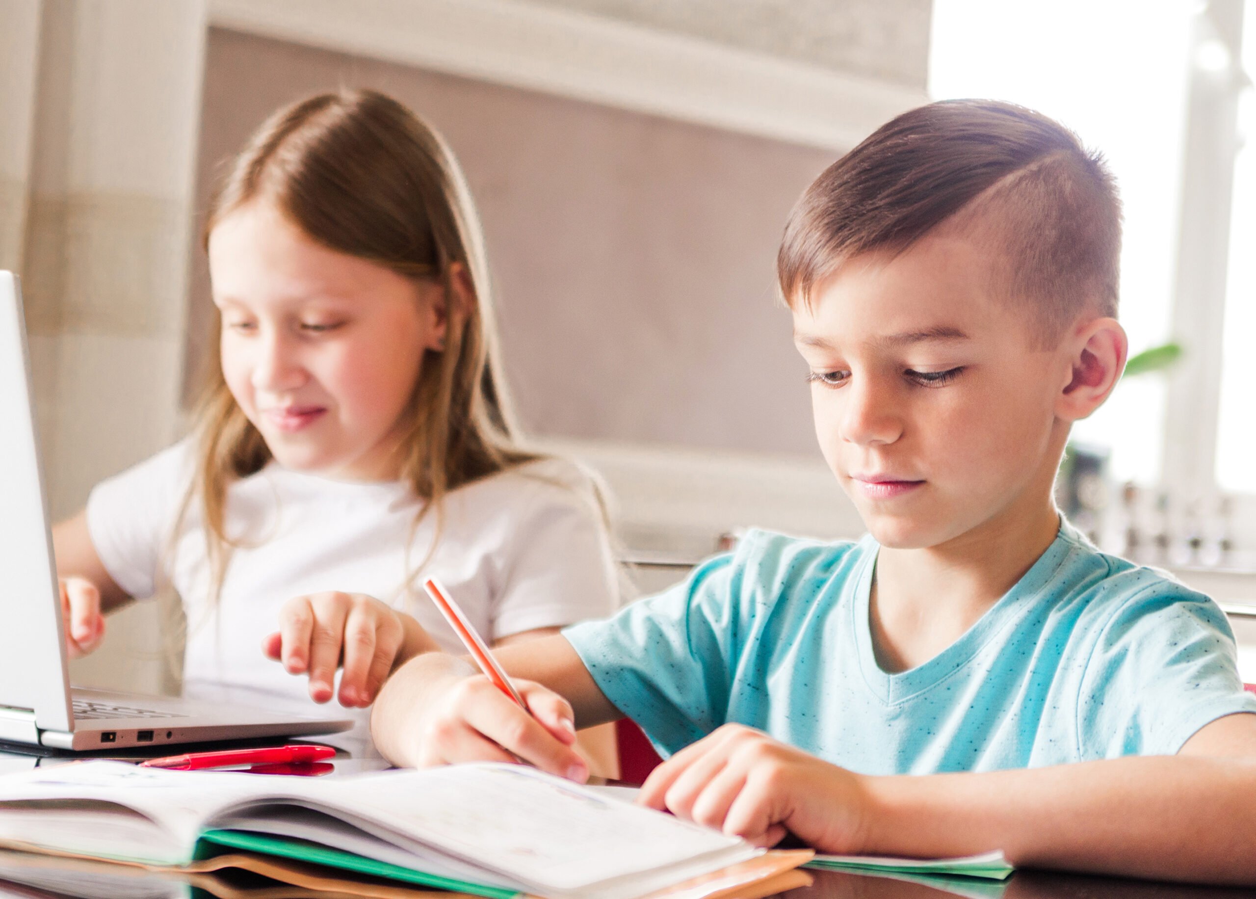 Boy and girl, brother and sister study at home. A girl watches a video lesson or an online conference, a boy does exercises in a notebook from a textbook