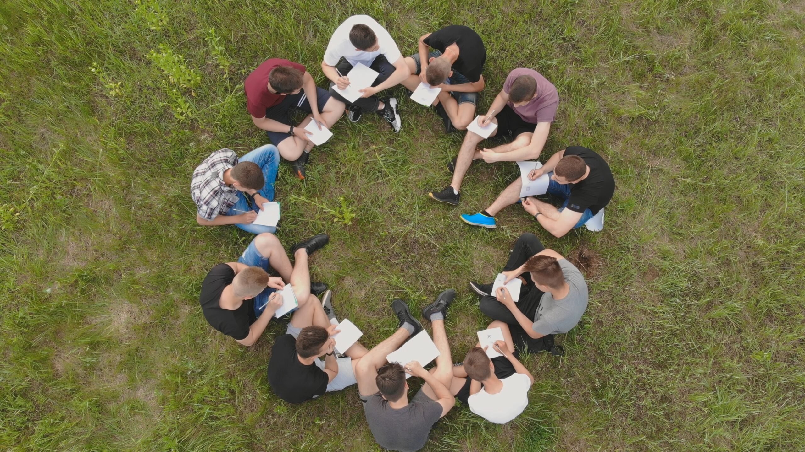 Teamwork concept. A group of high school students sit on the grass in a circle. Drone view