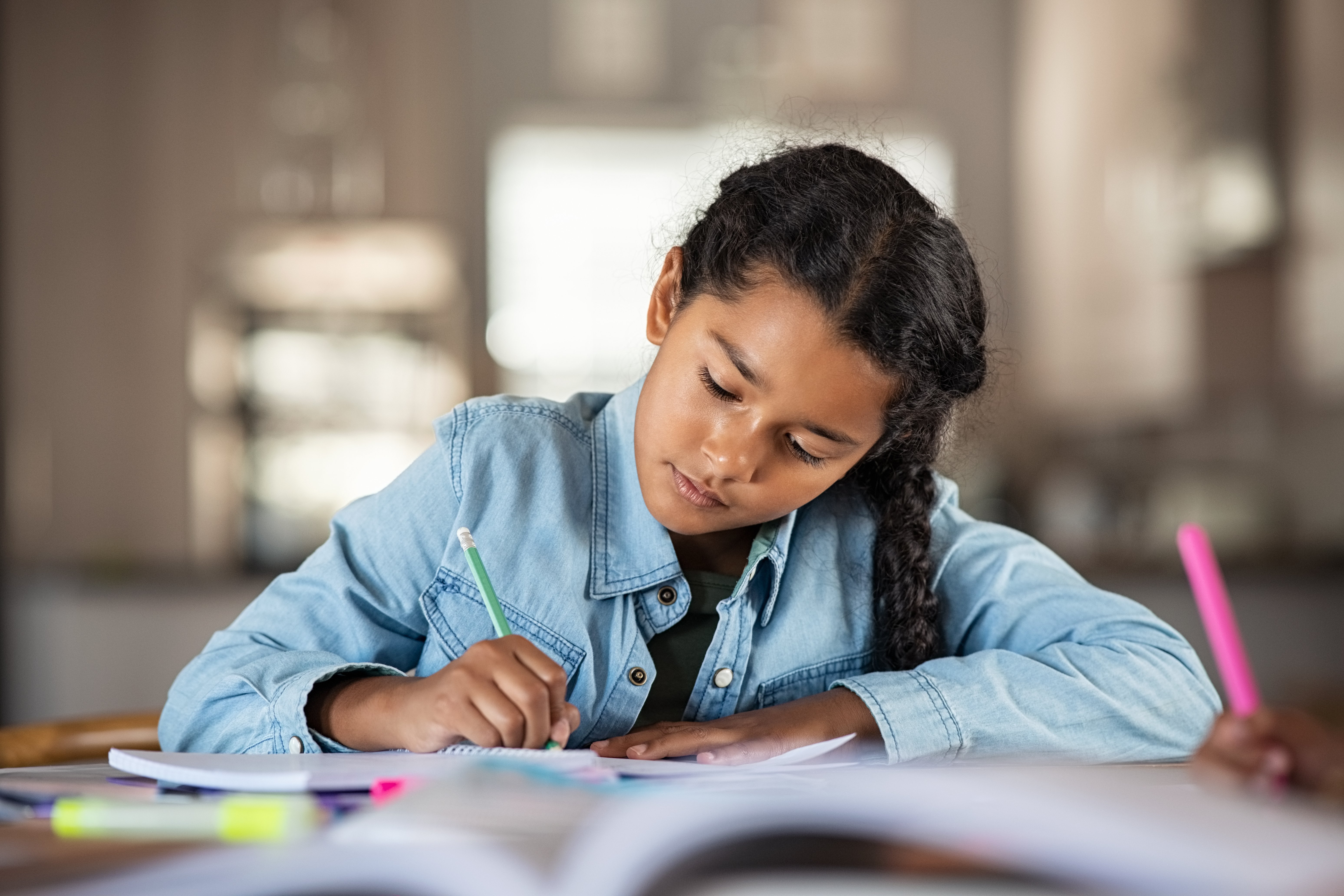 Middle eastern girl doing homework writing and reading at home. Concentrated beautiful indian female child writing in her notebook. Focused latin schoolgirl studying and preparing for exams.