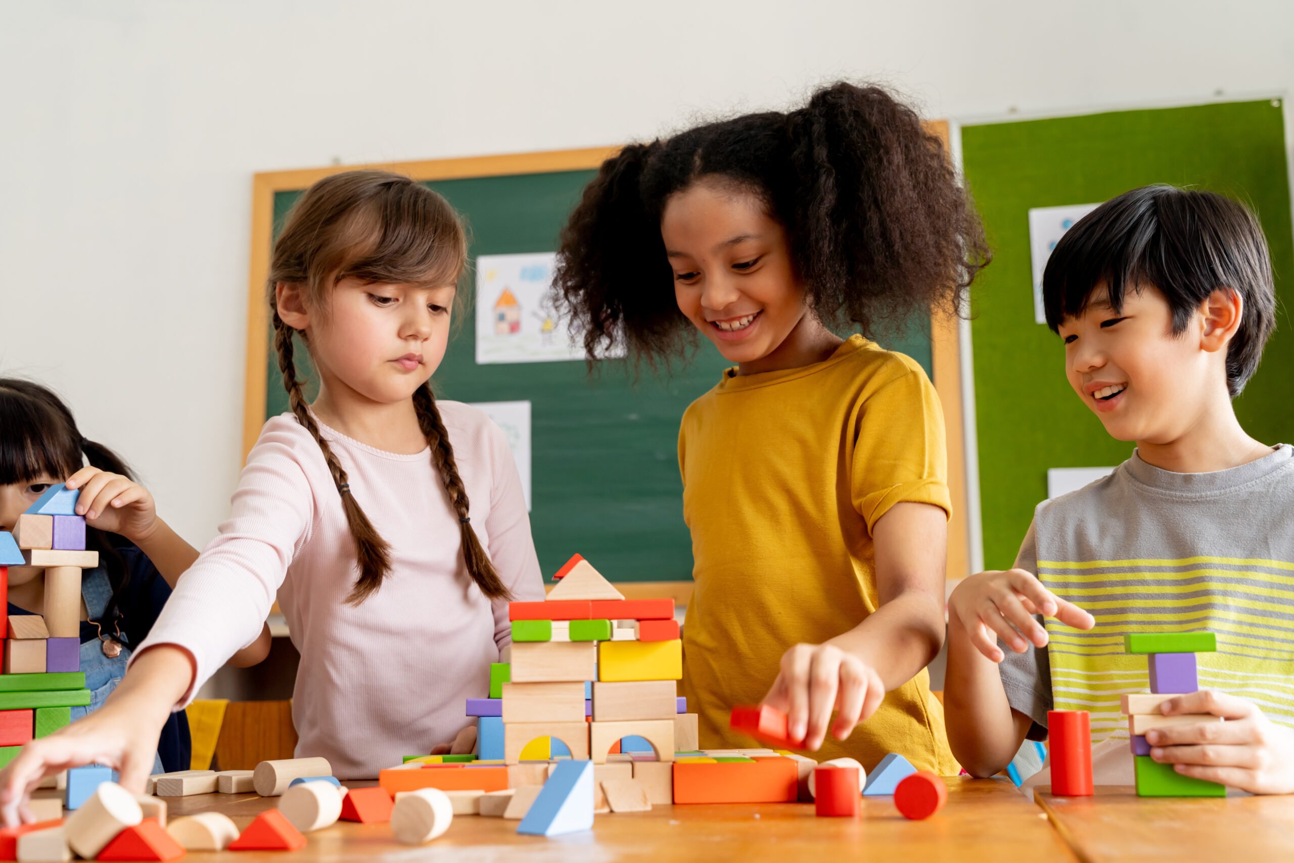 Group of multiethnic school friends using toy blocks in classroom, education, learning, teamwork. Children playing with wooden blocks in classroom