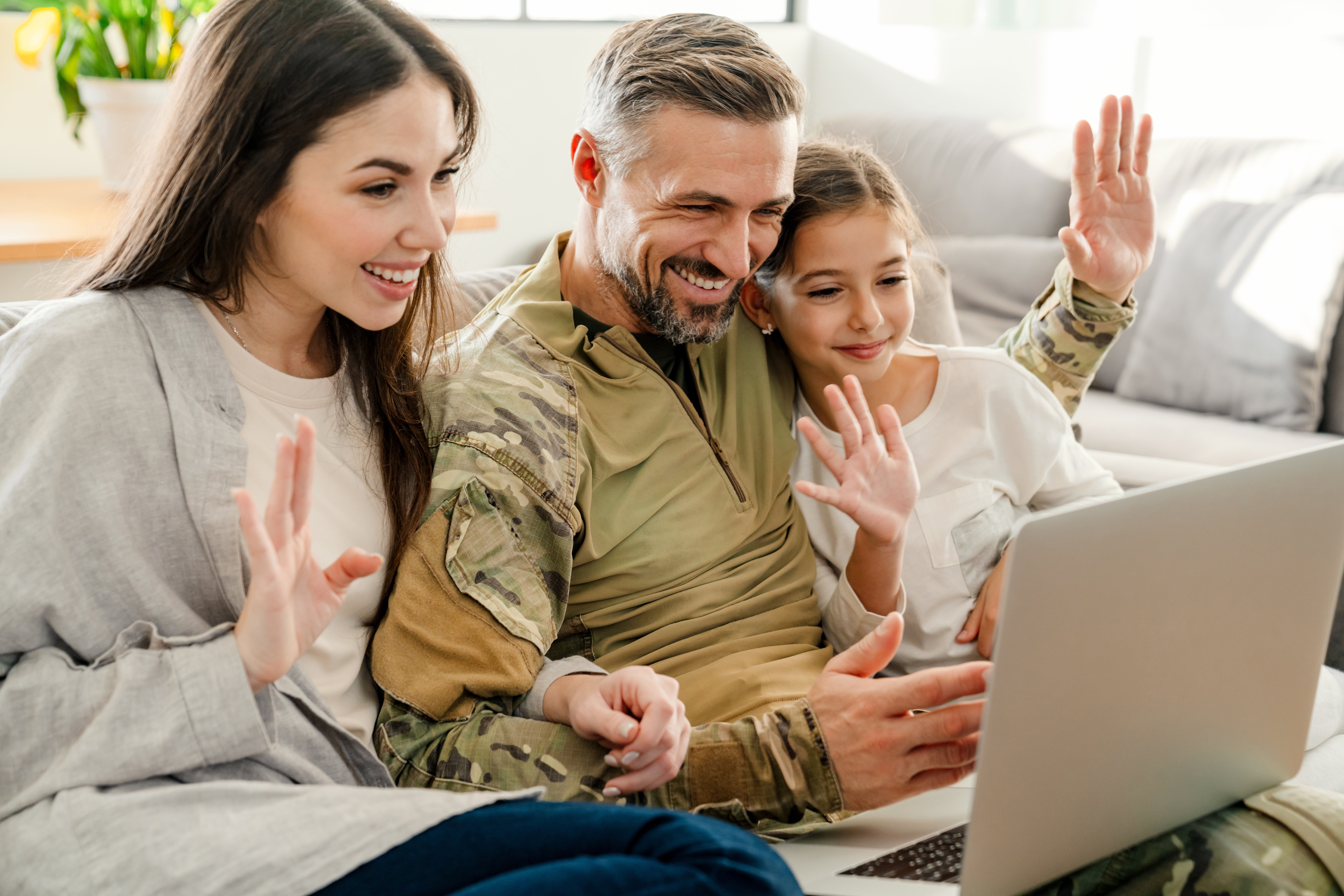 Happy military man waving hand with his family while using laptop indoors