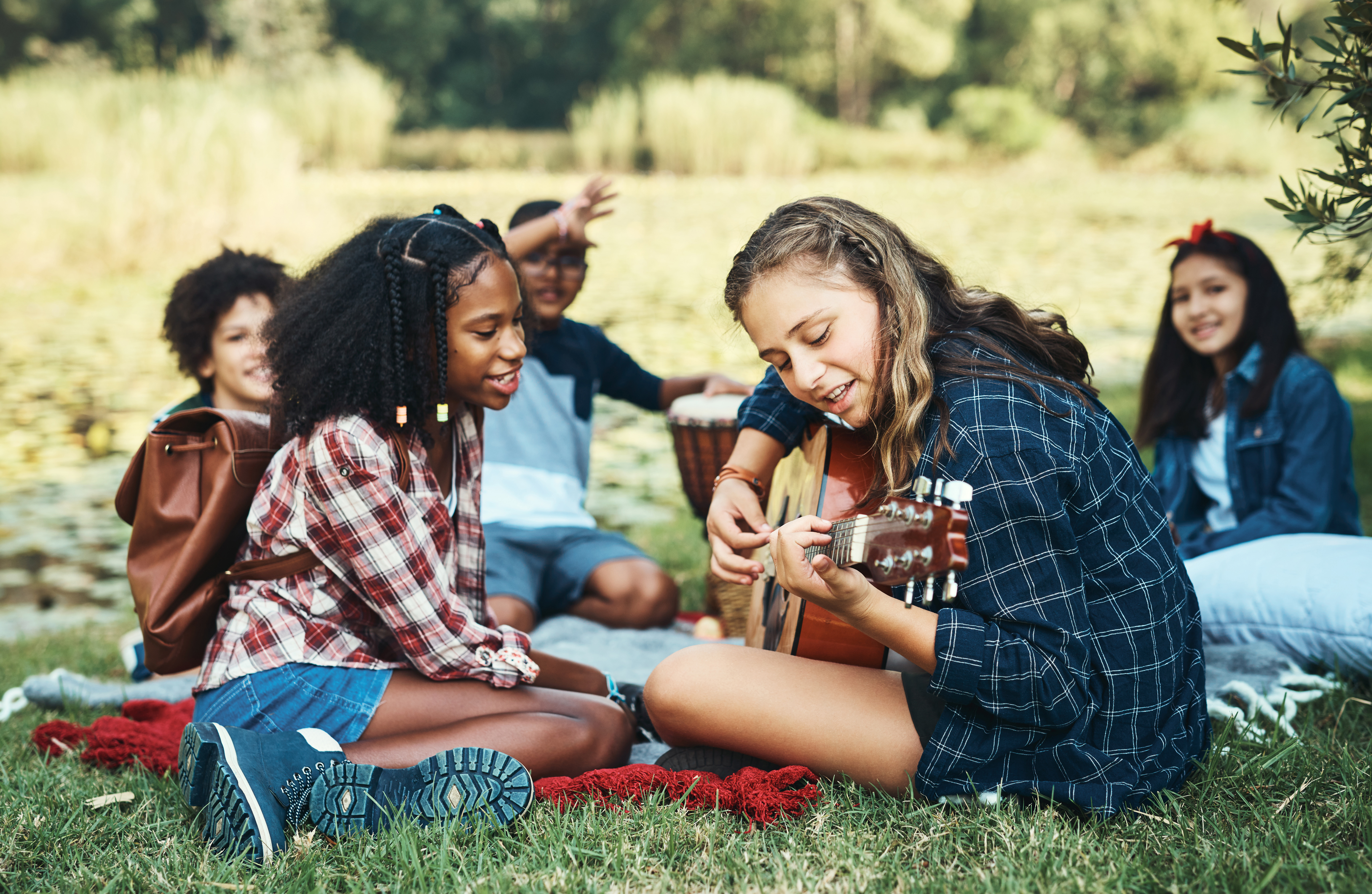 Shot of a group of teenagers playing musical instruments in nature at summer camp