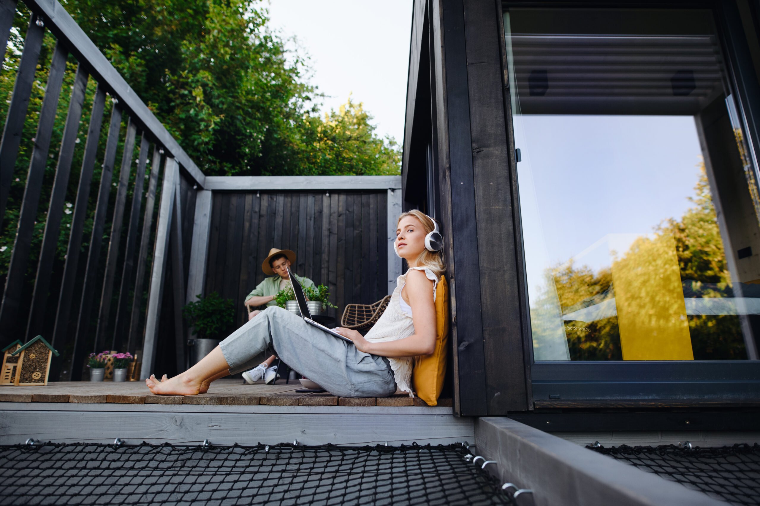 A happy young couple with laptop resting outdoors in a tiny house, weekend away and remote office concept.