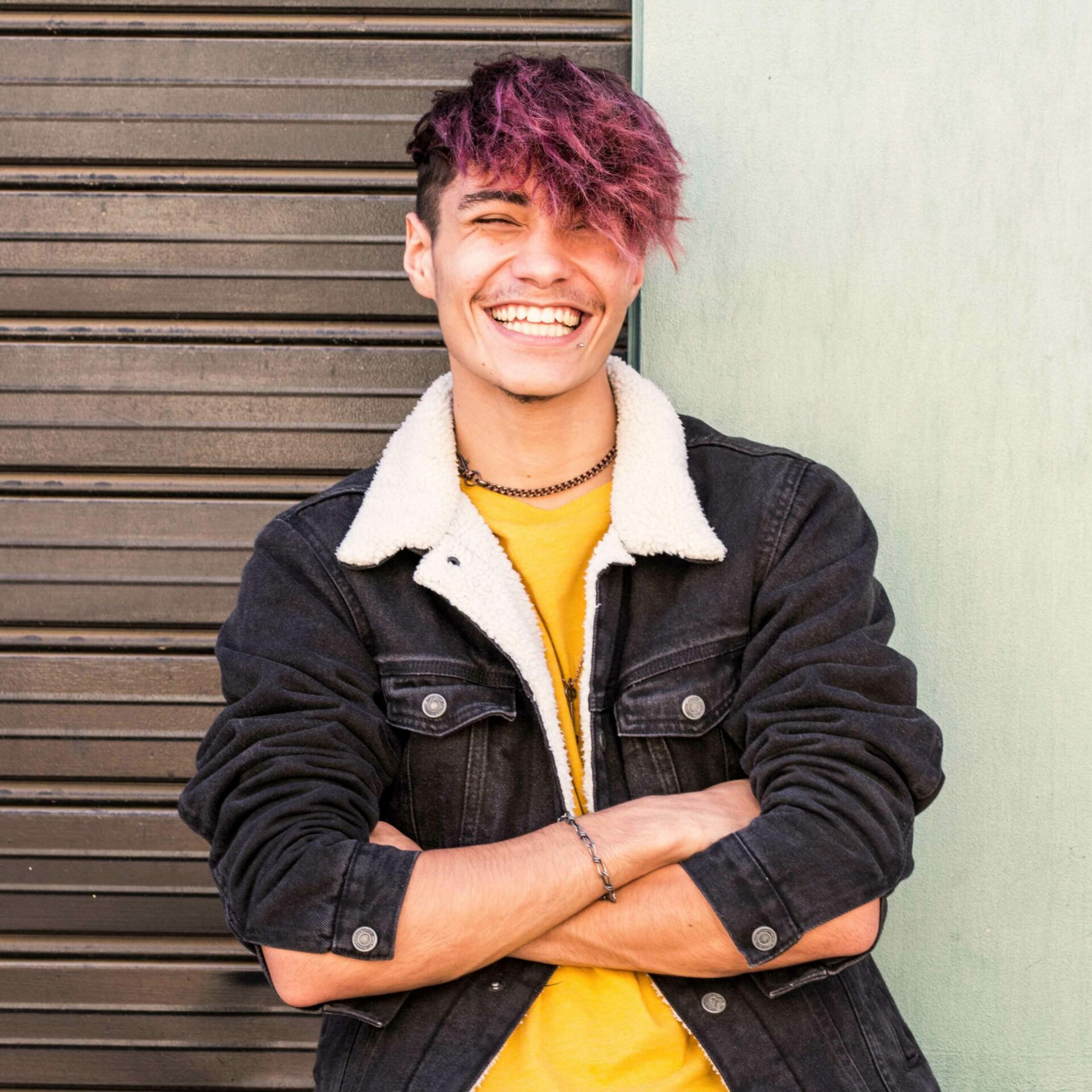 Boy with pink hair leaning against a wall