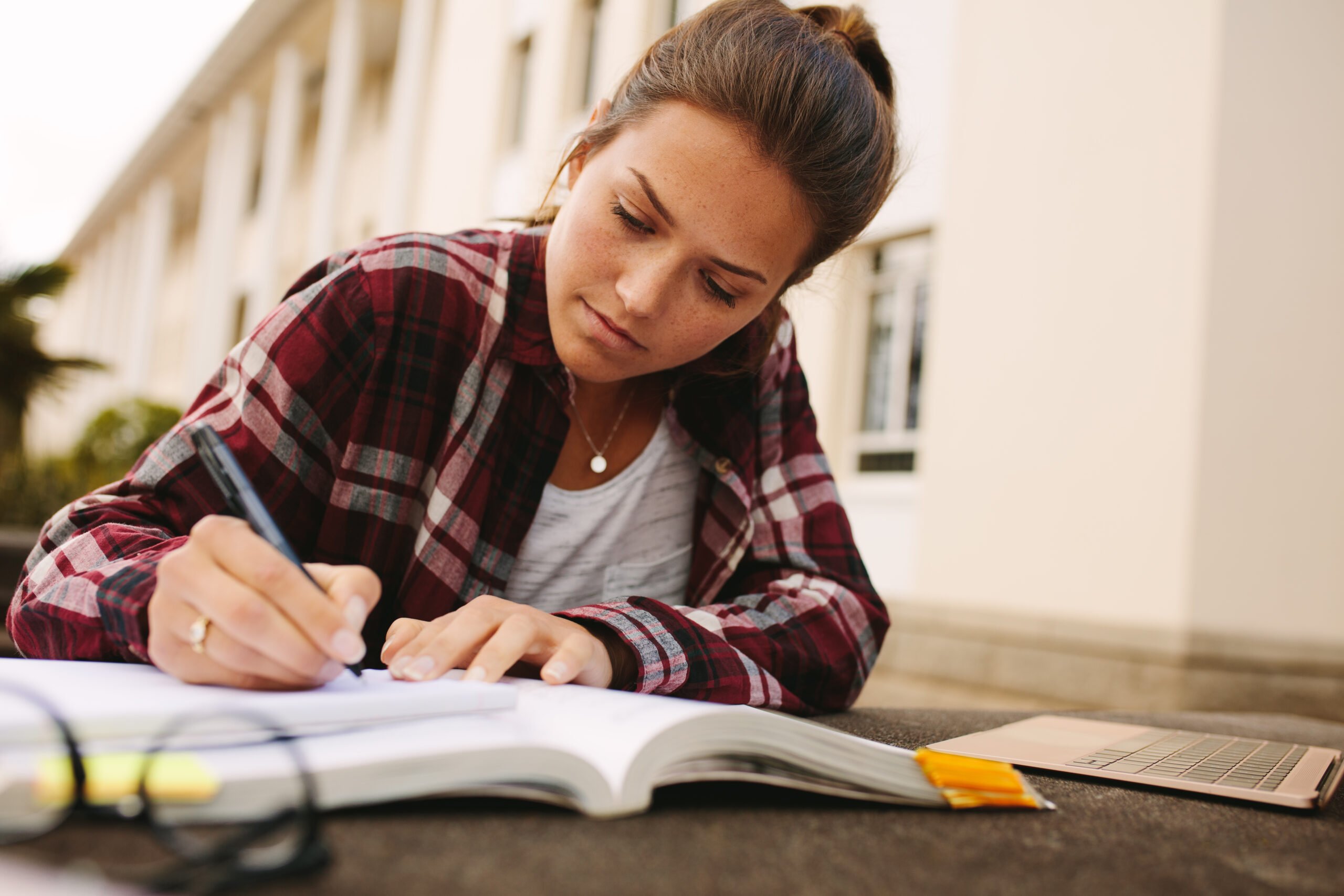 Female student sitting at college campus and making notes. Girl student studying at university campus.